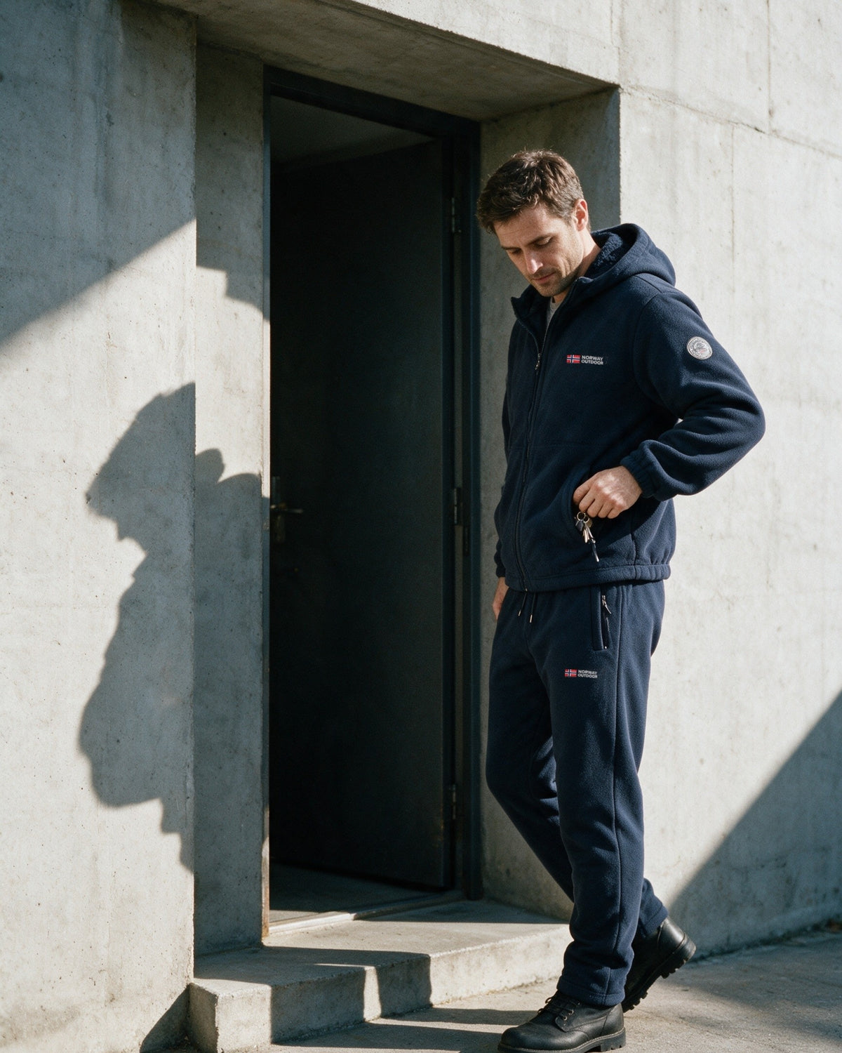 Man in the navy Norway fleece set by a concrete doorway